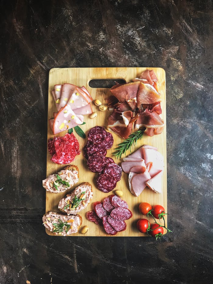 Delicious selection of cold cuts and bread on a wooden board with fresh herbs and tomatoes.